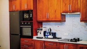 A kitchen with wooden cabinets, a black refrigerator, a microwave, an oven, a coffee maker, and a stove. - Goba Peaks (Dar es Salaam)