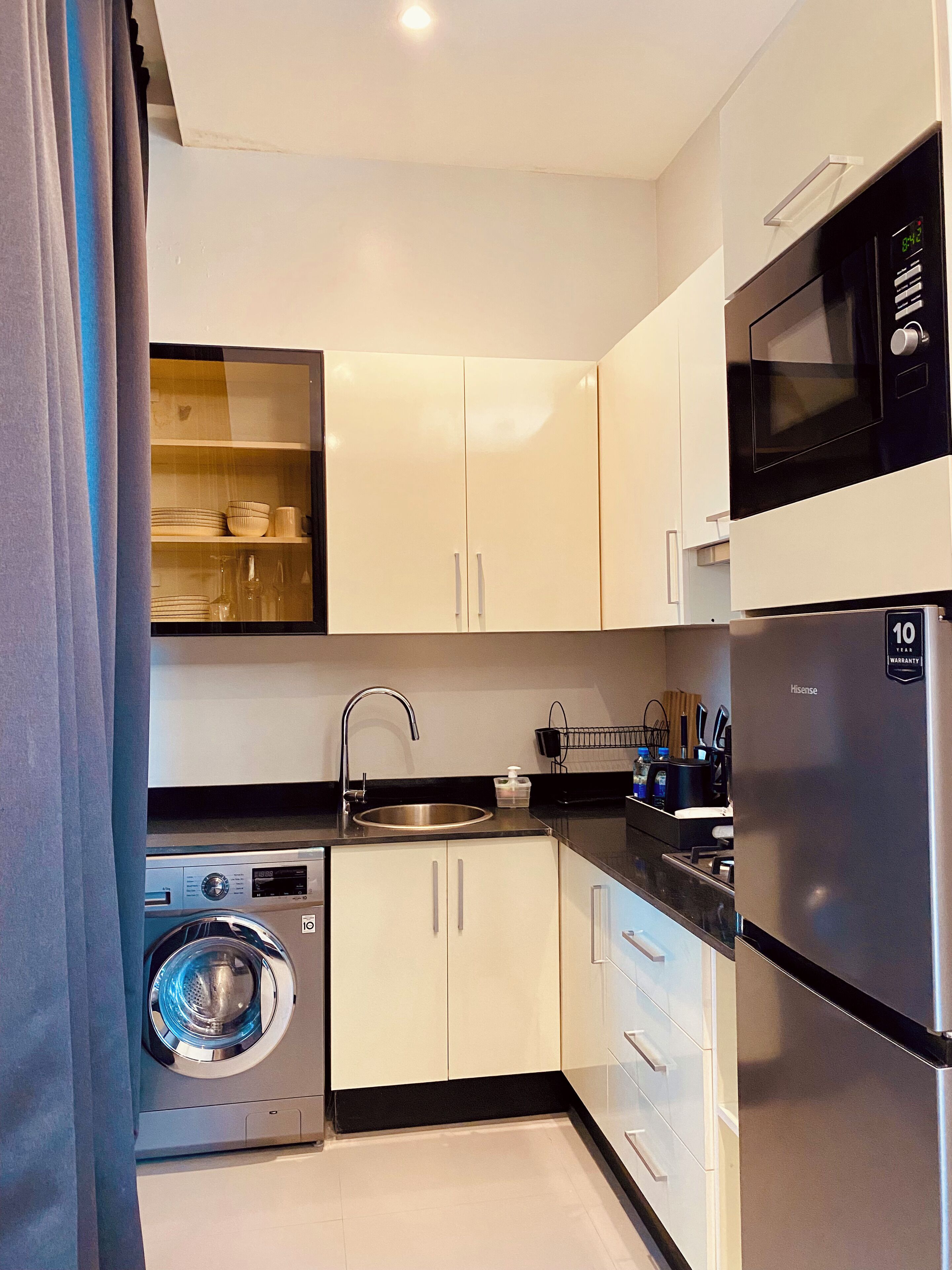 A compact kitchen with a washing machine, a sink, and a microwave.