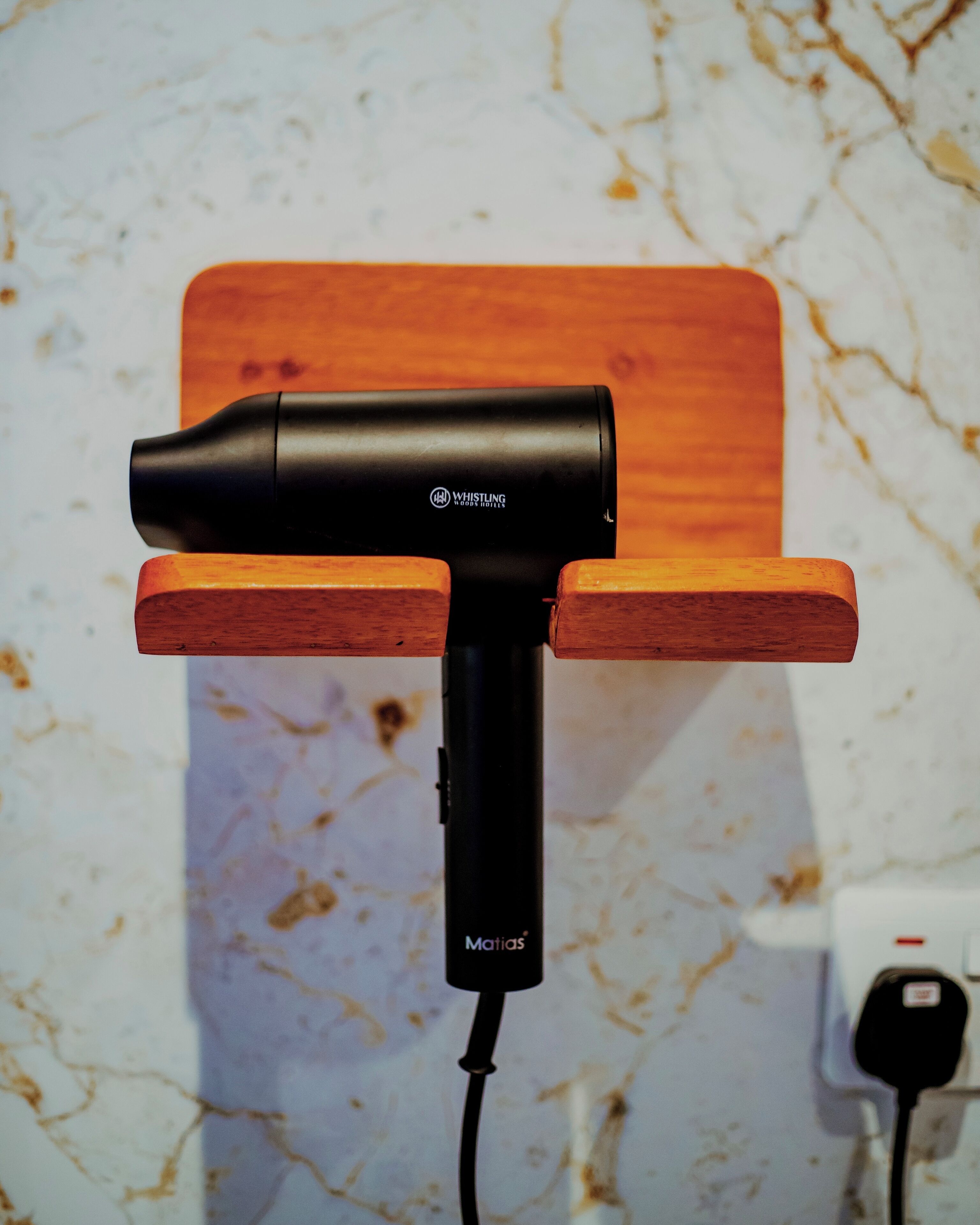 A black hairdryer mounted on a wooden stand against a marble wall.