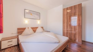 A modern bedroom with a wooden headboard, a large bed with white bedding, two bedside tables, and a wooden wardrobe. - Family and pet-friendly apartment in beautiful Flachau. (Flachau)