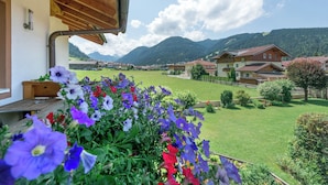 A balcony with a wooden railing overlooking a green lawn and a village with houses and mountains in the background. - Family and pet-friendly apartment in beautiful Flachau. (Flachau)
