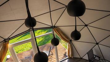 Una estructura tipo tienda con terraza de madera, lámparas esféricas colgantes y vistas a una zona verde.