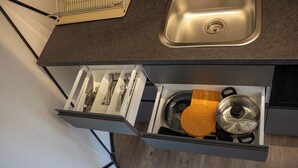 Uma gaveta de cozinha com utensílios, uma tábua de corte e uma panela.