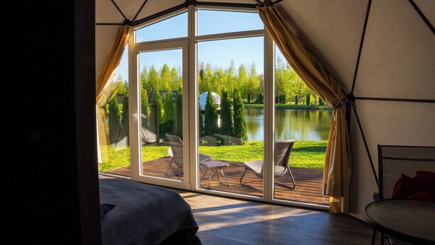 Alojamento em tenda com uma grande porta de vidro que dá para um deck exterior com cadeiras e uma mesa.