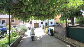 Una calle estrecha con una moto estacionada, una hilera de botes de basura de colores y varias casas al fondo.