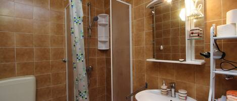 Une salle de bain équipée d’une douche, de toilettes, d’un lavabo et d’étagères où sont rangés les produits de toilette.