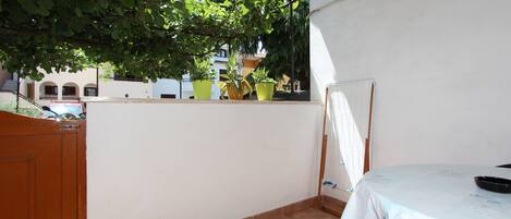 A balcony with potted plants, a table with a tablecloth, and a view of buildings in the background.