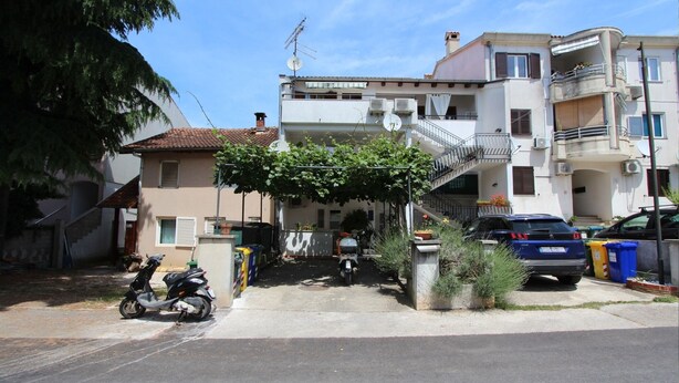 A residential building with a covered entrance, a scooter parked outside, and a blue car parked in the driveway. - Studio Vera (Rovinj)