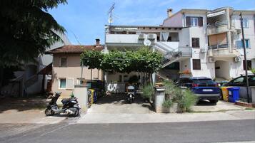 Un edificio residencial con un acceso cubierto, una moto estacionada afuera y un auto azul en la entrada.