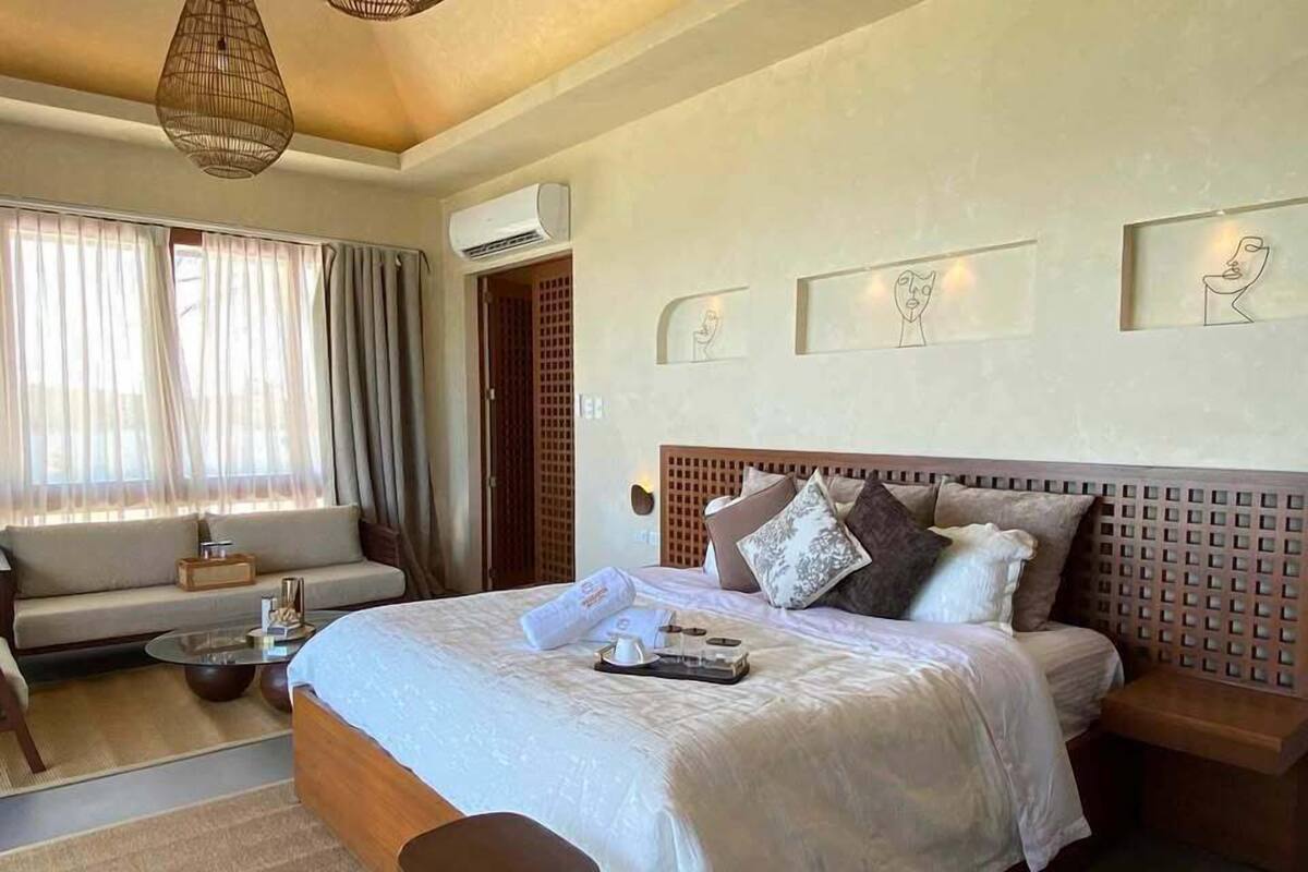 Een moderne hotelkamer met een groot bed, een slaapbank, een klein tafeltje en een raam met gordijnen.