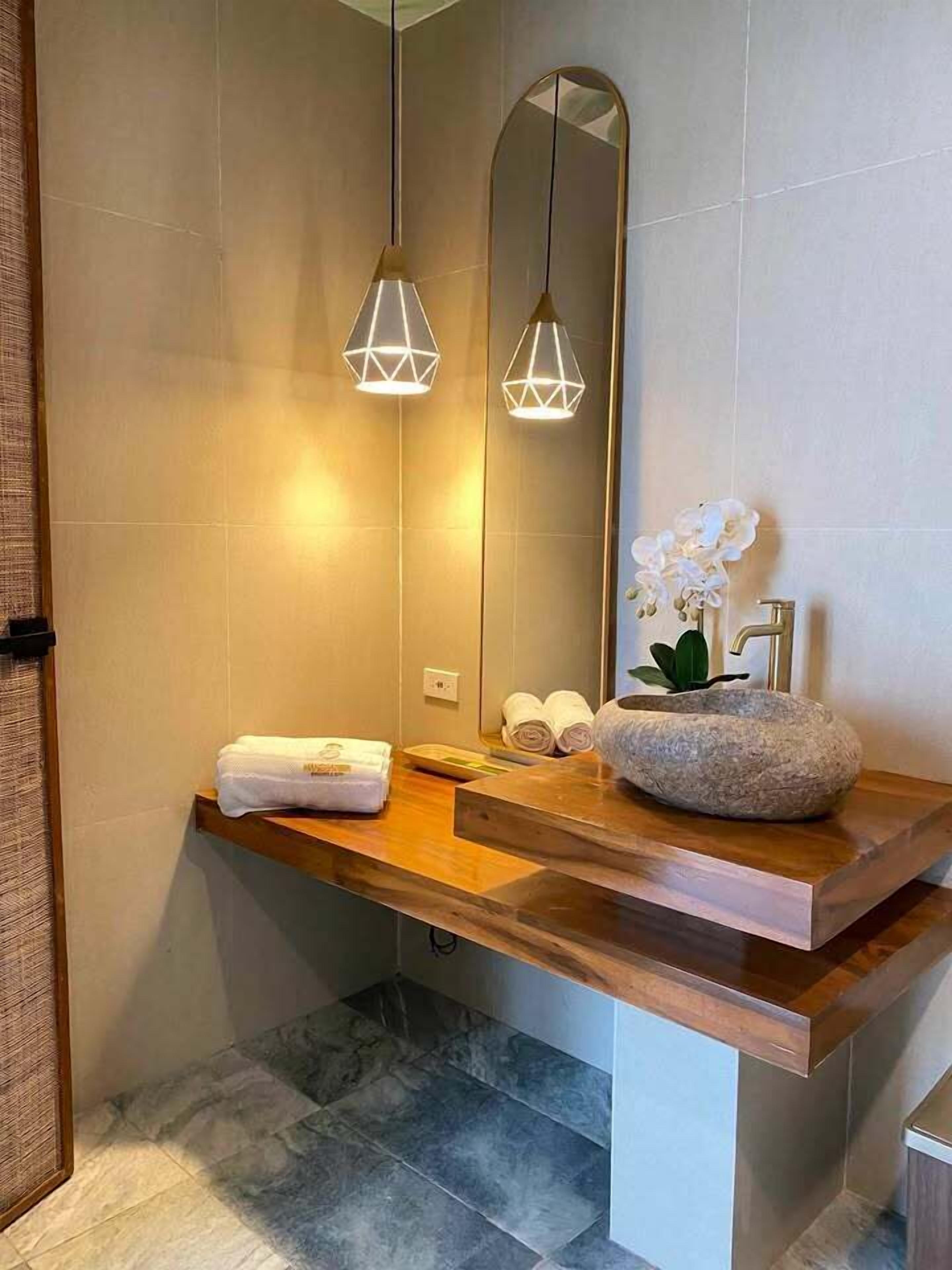 A modern bathroom with a wooden vanity, a large mirror, and two pendant lights.