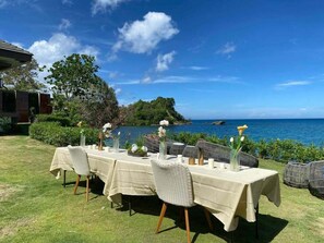 Un espace de restauration en plein air, avec des tables dressées pour un repas, offrant une vue sur une étendue d’eau et un paysage montagneux.