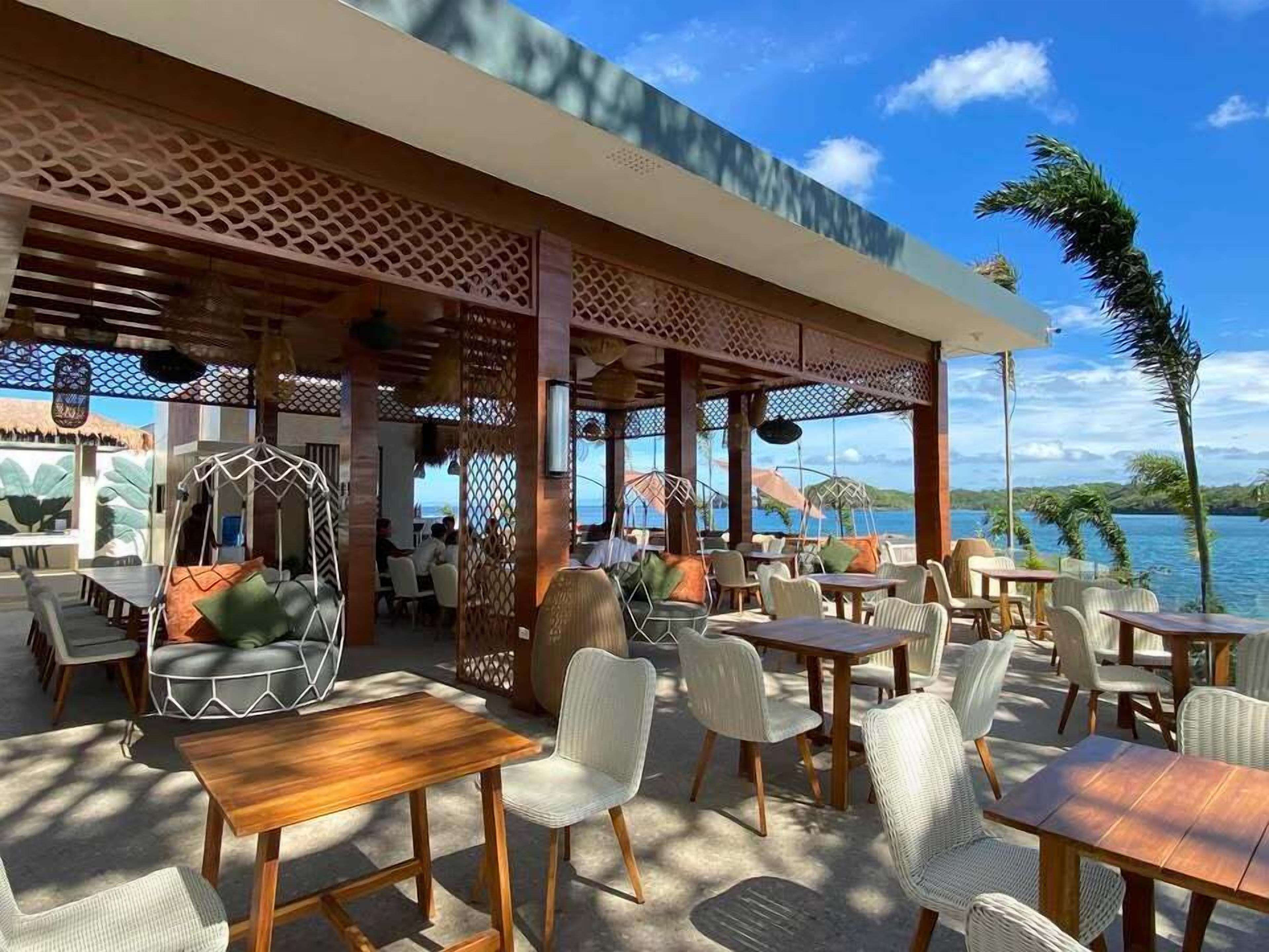 An outdoor seating area with tables and chairs, a wooden pergola, and a view of the sea.
