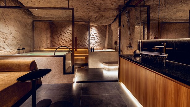 A modern bathroom with a stone wall, a bathtub, a sink, and a wooden vanity. - KiN Hotel Onsen  (Ho Chi Minh City)