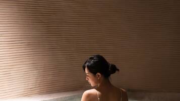 A person in a bathtub with a textured wall and a visible ceiling vent.