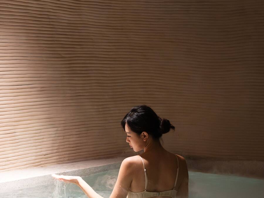 A person in a bathtub with a textured wall and a visible ceiling vent.