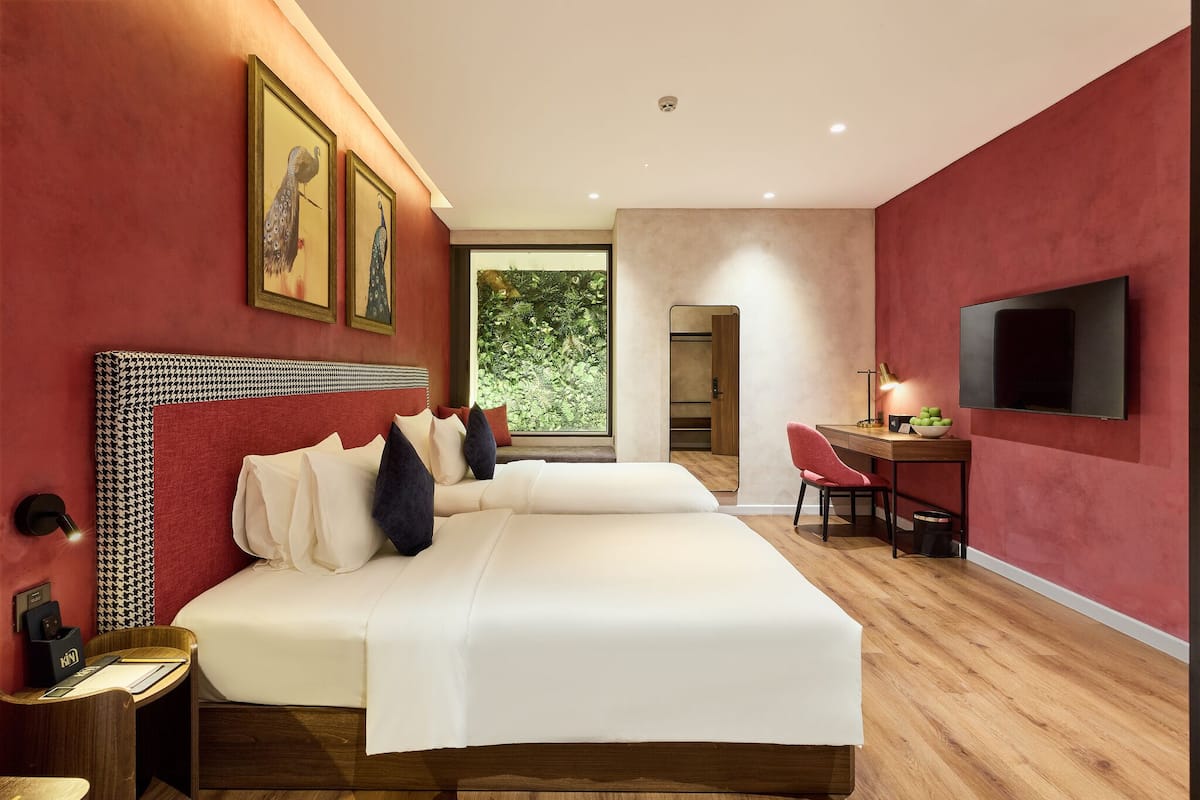 A modern hotel room with a large bed, a desk with a chair, a television, and artwork on the walls.