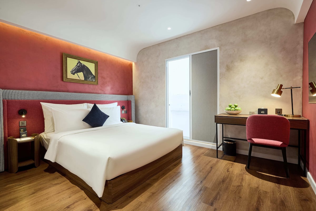A modern hotel room with a large bed, a desk, and a chair. There is a window with a view of the city.