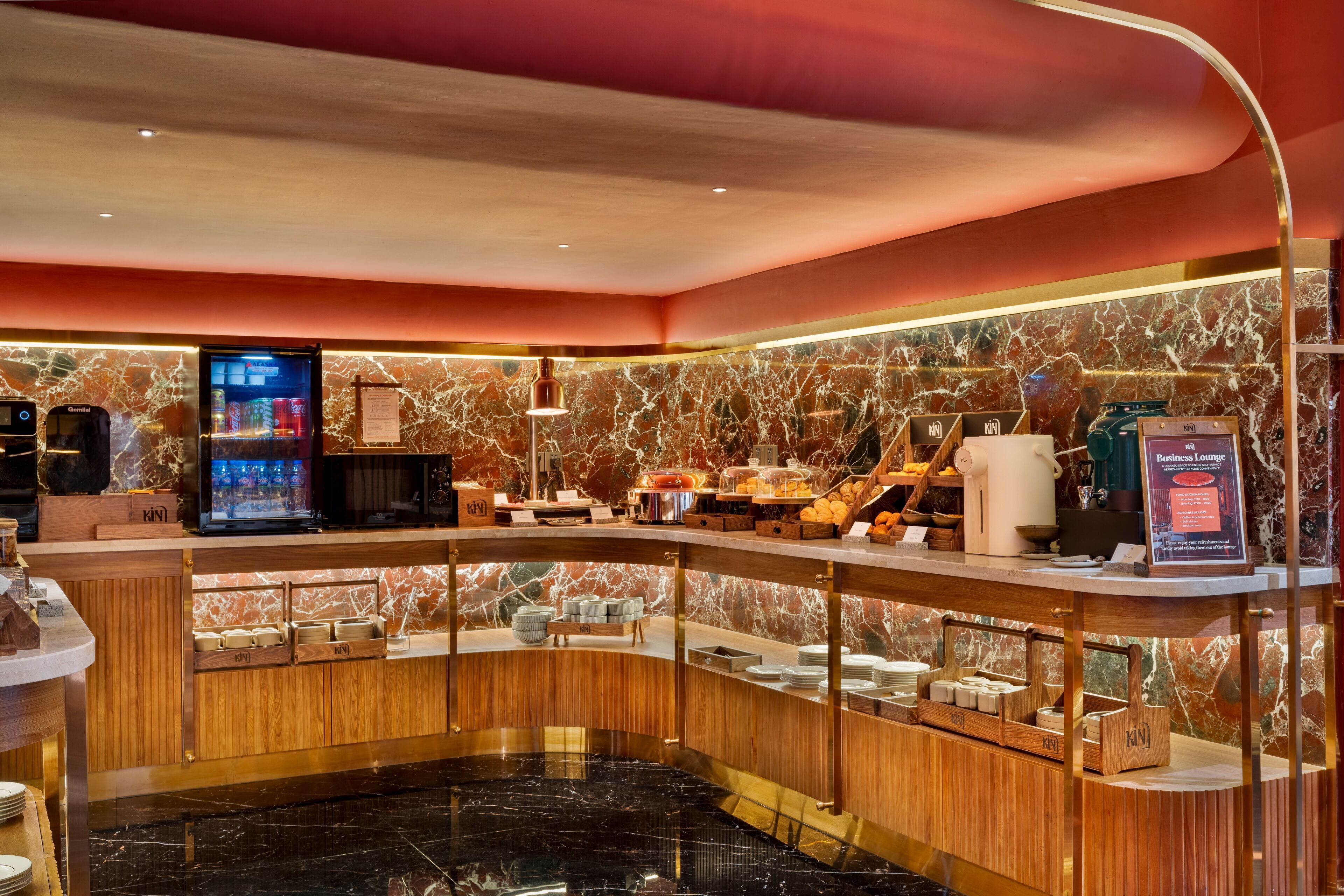 A hotel lobby with a marble wall, a reception desk, a coffee machine, and a business lounge sign.