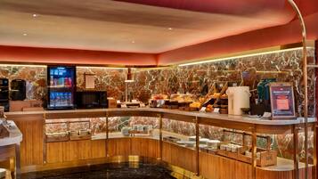 A hotel lobby with a marble wall, a reception desk, a coffee machine, and a business lounge sign.