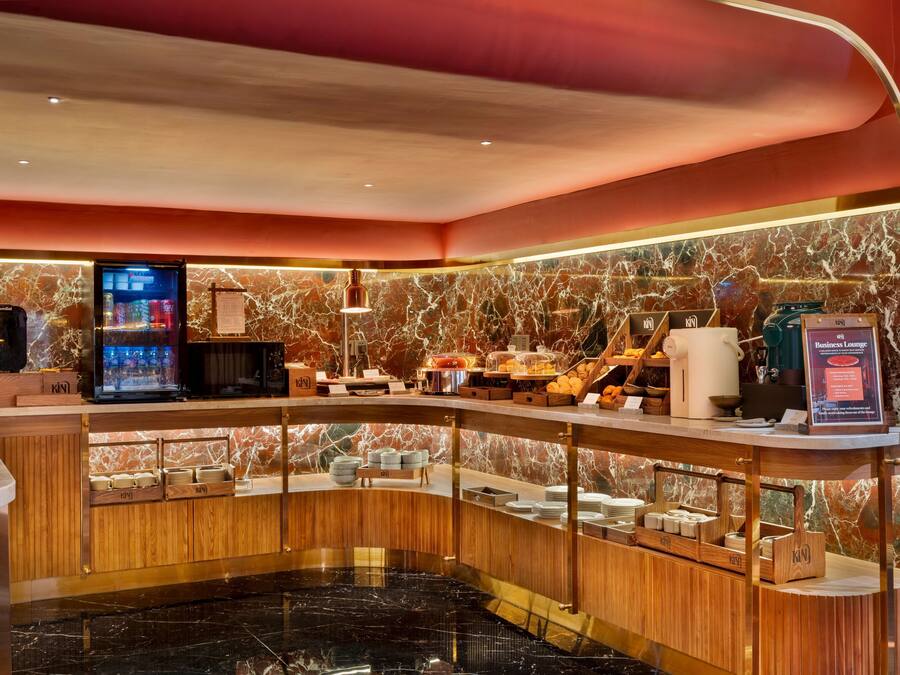 A hotel lobby with a marble wall, a reception desk, a coffee machine, and a business lounge sign.