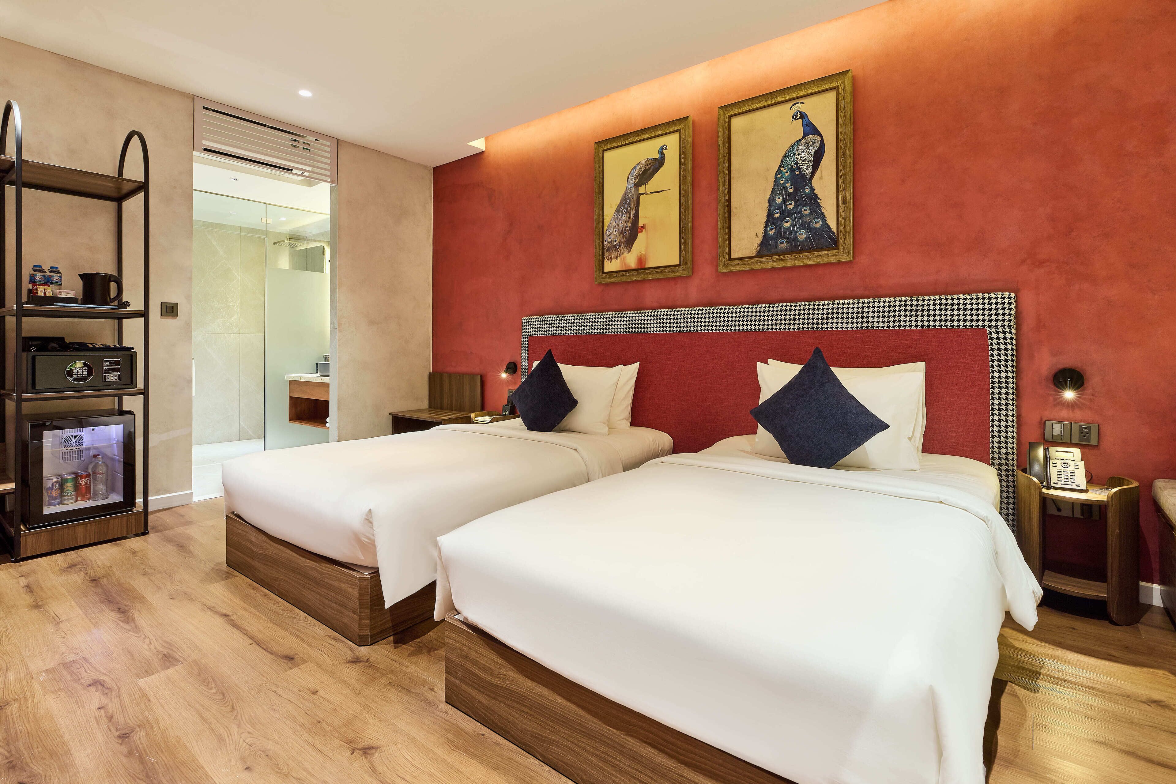 A hotel room with two beds, a minibar, a glass shower enclosure, and artwork on the walls.
