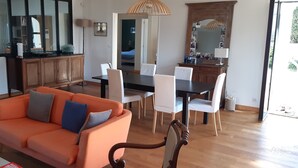 Een woonkamer met een oranje bank, een eettafel met stoelen, een houten kast en een grote spiegel.