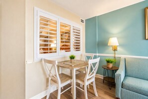 Uma área de refeições com mesa e cadeiras, uma janela com persianas, um abajur e um sofá.