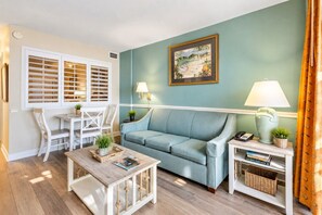 Sala de estar com sofá azul claro, cadeiras brancas, mesa de centro de madeira e um quadro na parede.