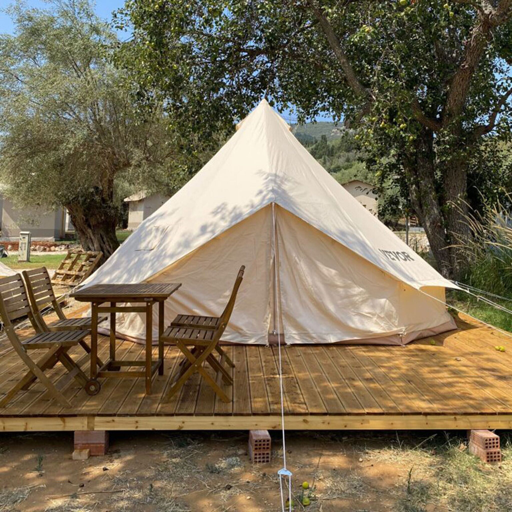 A large, white tent with the word "TENT" on it, set up on a wooden deck with two wooden chairs and a table.