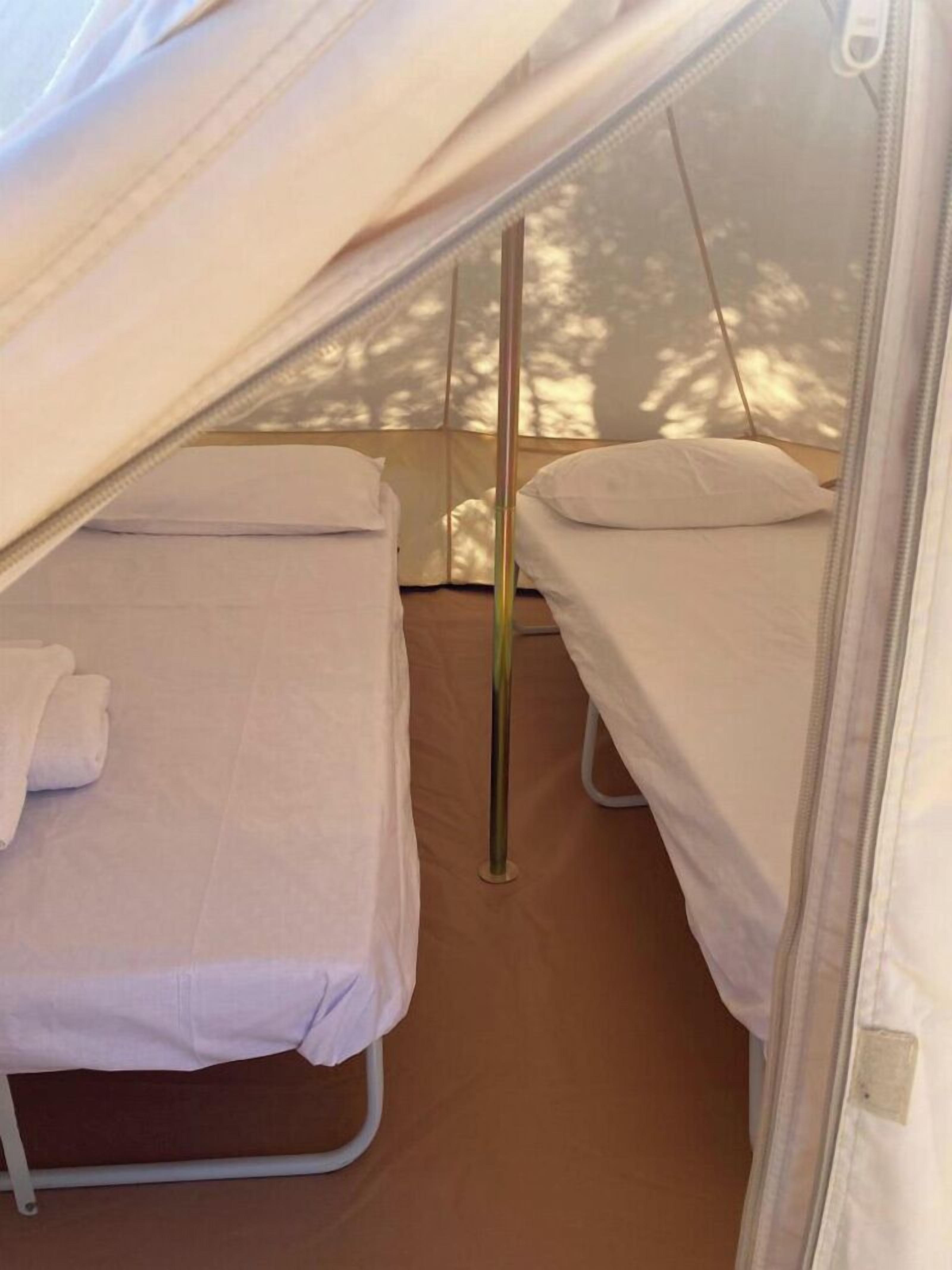 Uma tenda com duas camas, cada uma com um travesseiro e um cobertor dobrado.