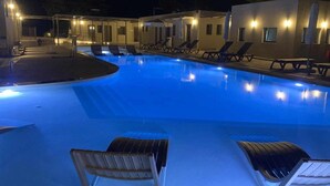 A swimming pool with lounge chairs and a covered area at night. - Nirikos Camping (Lefkada)