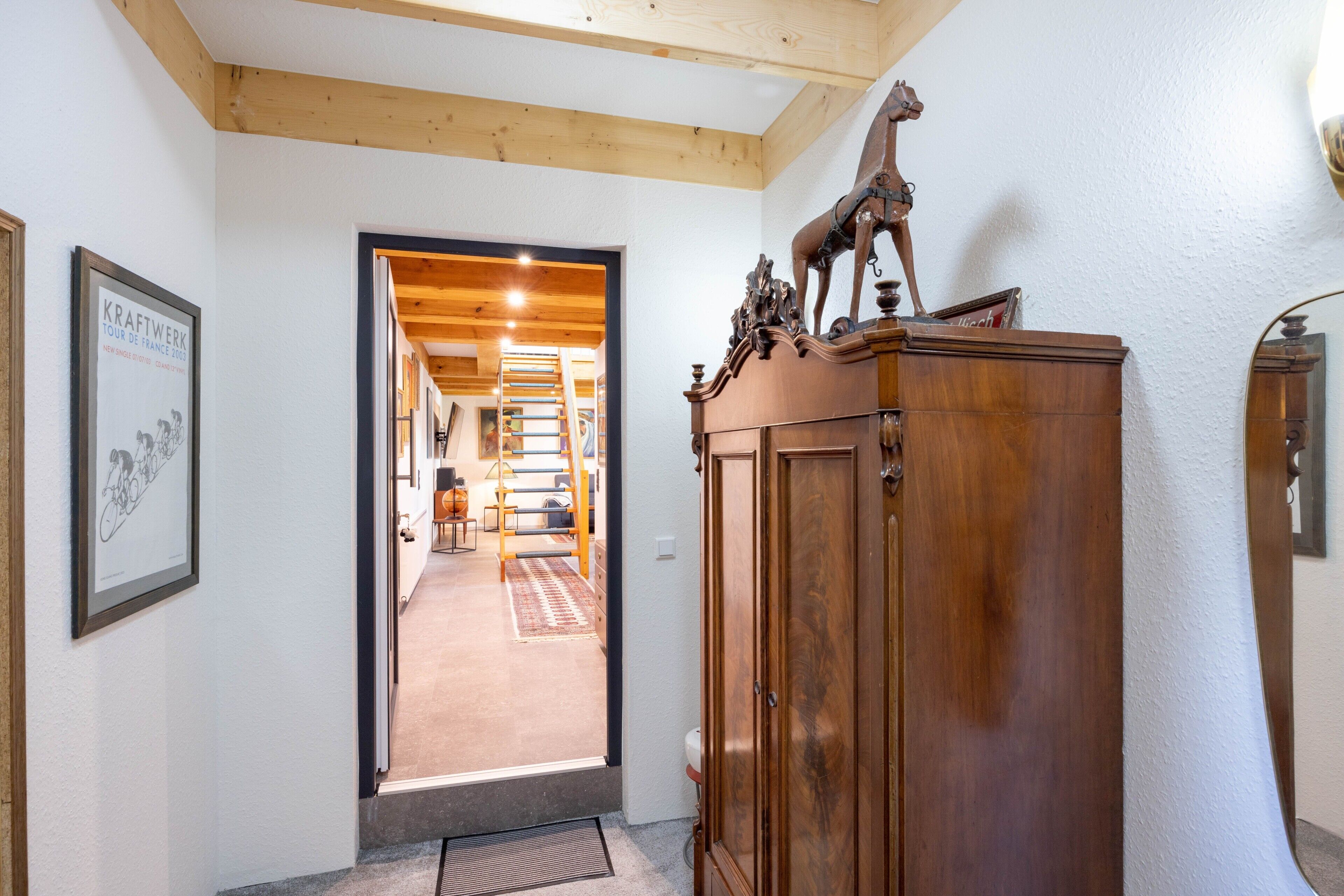A hallway with a wooden cabinet, a framed picture, and a staircase leading to another room.