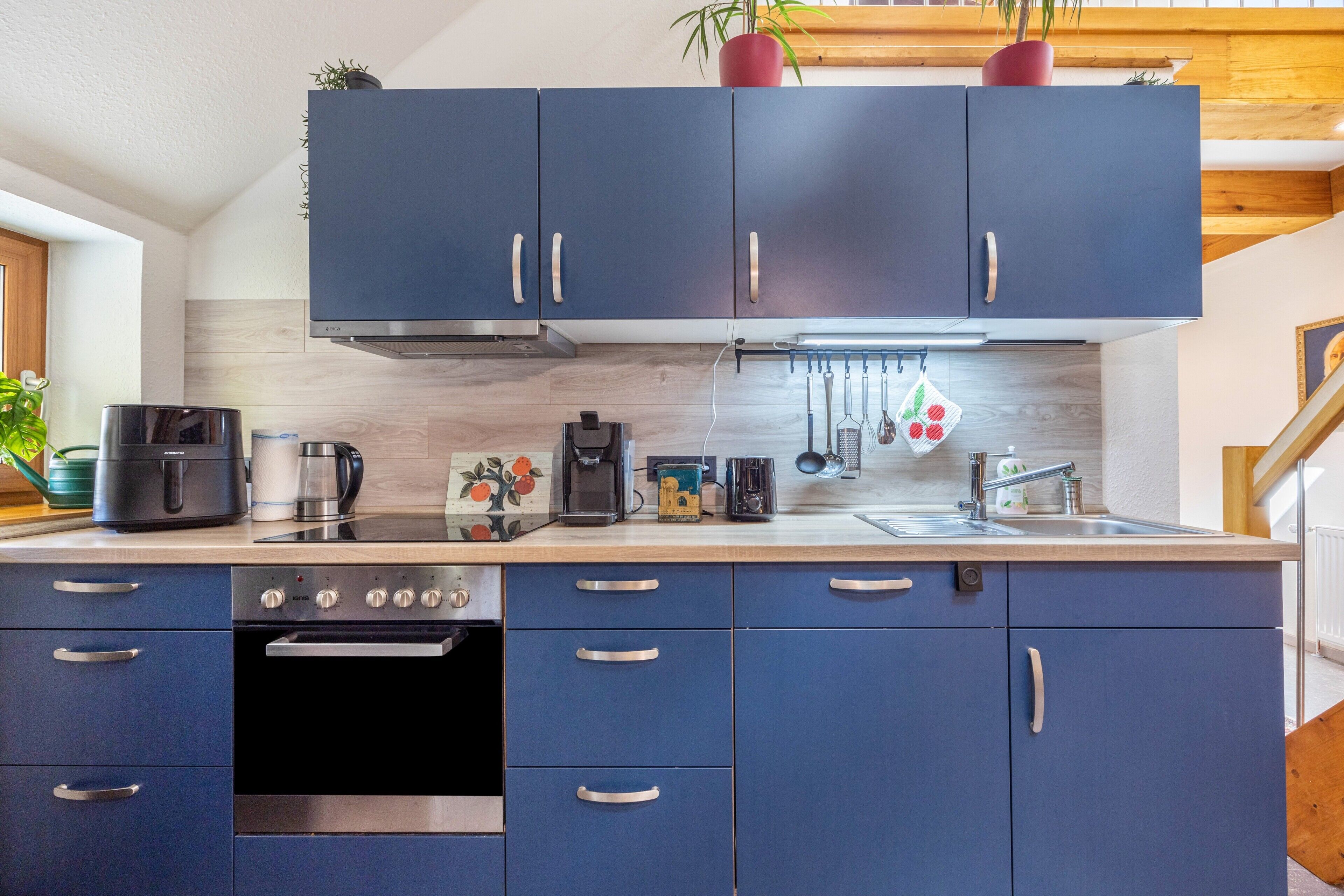 A modern kitchen with blue cabinets, a built-in oven, and a stainless steel range hood.