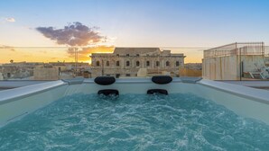 A rooftop pool with two black loungers, a view of a historic building, and a sunset in the background. - La Dimora di San Nicola (Syracuse)