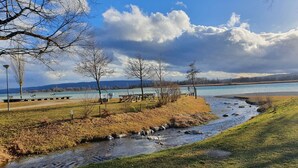 A riverside park with picnic tables, a walking path, and a view of a lake. - Casa di Napolitano at Lake Constance – Modern Attic Apartment Near the Lake (Radolfzell am Bodensee)