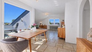 A spacious dining area with a wooden table and chairs, a vase with flowers, and a view of the outdoors. - Casa di Napolitano at Lake Constance – Modern Attic Apartment Near the Lake (Radolfzell am Bodensee)