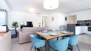 A modern living room with a sofa, TV, and dining area with chairs and a table set for two. - Terrazza Beach Golf (Loulé)