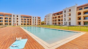 A modern hotel with a central swimming pool, multiple balconies, and a wooden deck area. - Terrazza Beach Golf (Loulé)