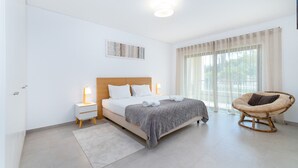 A modern bedroom with a bed, bedside tables, a chair, and a large window. - Terrazza Beach Golf (Loulé)
