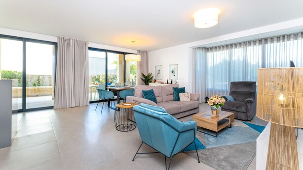 A modern living room with a sofa, armchairs, and a coffee table. There is a dining area with a table and chairs, and a balcony with curtains. - Terrazza Beach Golf (Loulé)