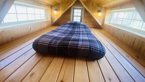 Une chambre mansardée avec un plafond haut, un plancher en bois et deux fenêtres.