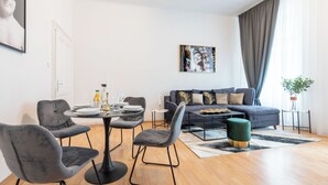 Ett modernt vardagsrum med en matplats, grå möbler med tygklädsel, en grå soffa med dekorativa kuddar, ett runt soffbord och ett litet sidobord med en växt.
