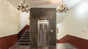 A marble-floored hallway with a staircase, a wall-mounted elevator, and two chandeliers. - Treebo Basera (Mathura)
