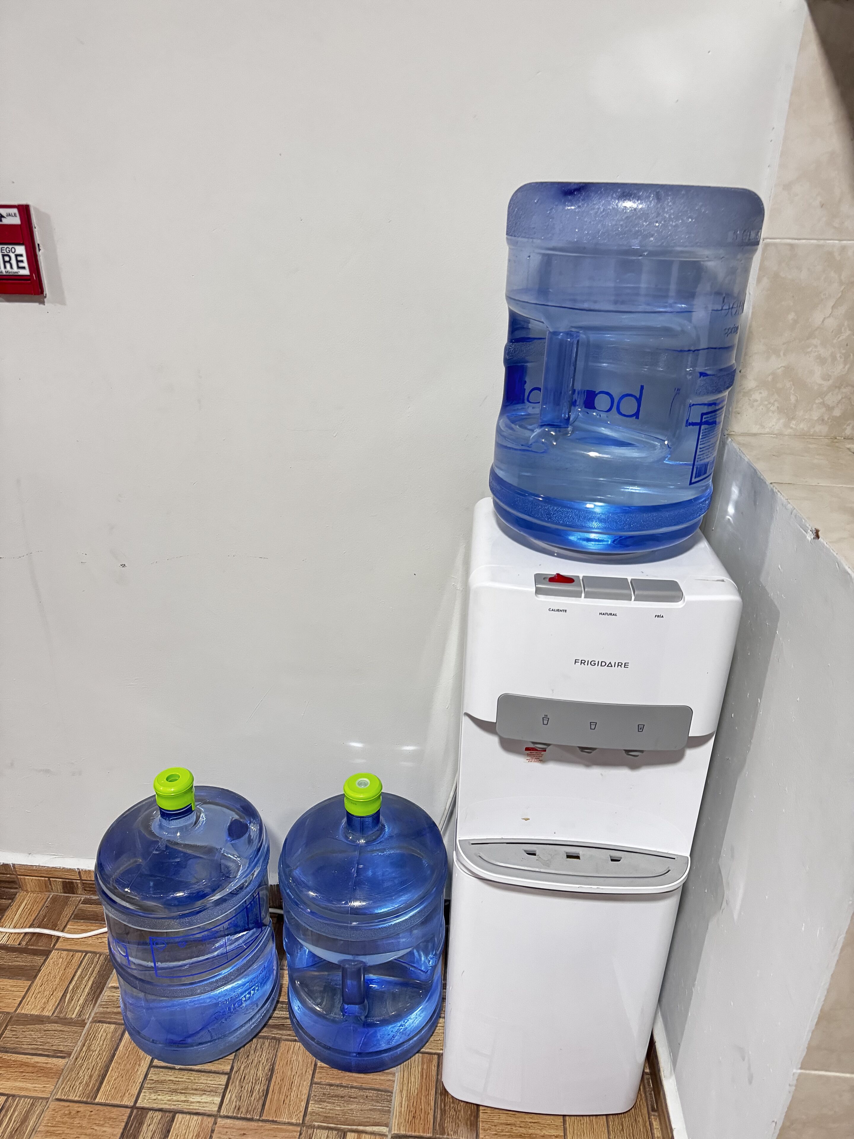 A water dispenser and two water jugs on a tiled floor.