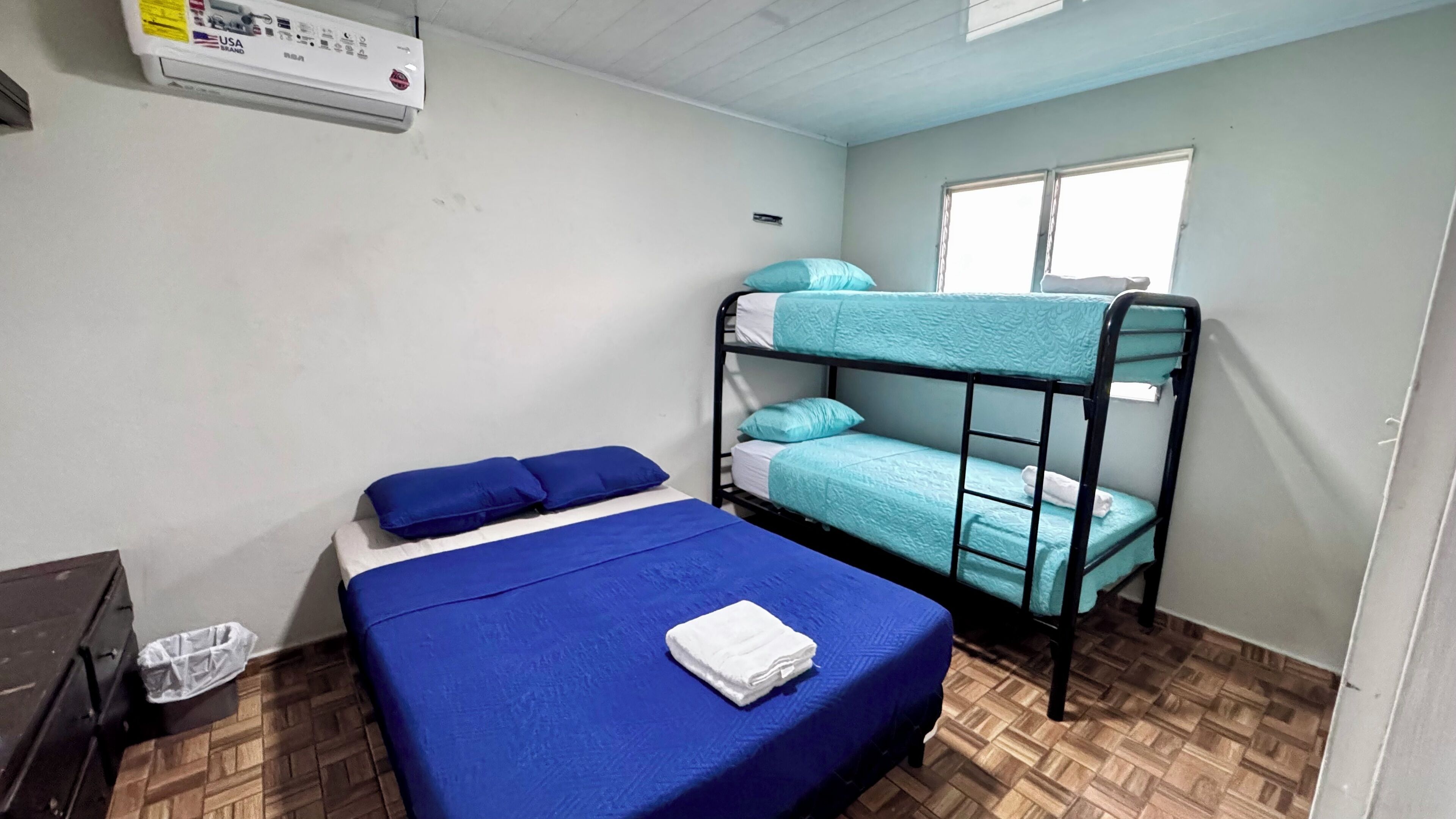 A dormitory room with bunk beds, a single bed, a heater, and a window.