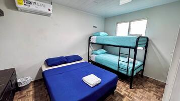A dormitory room with bunk beds, a single bed, a heater, and a window.