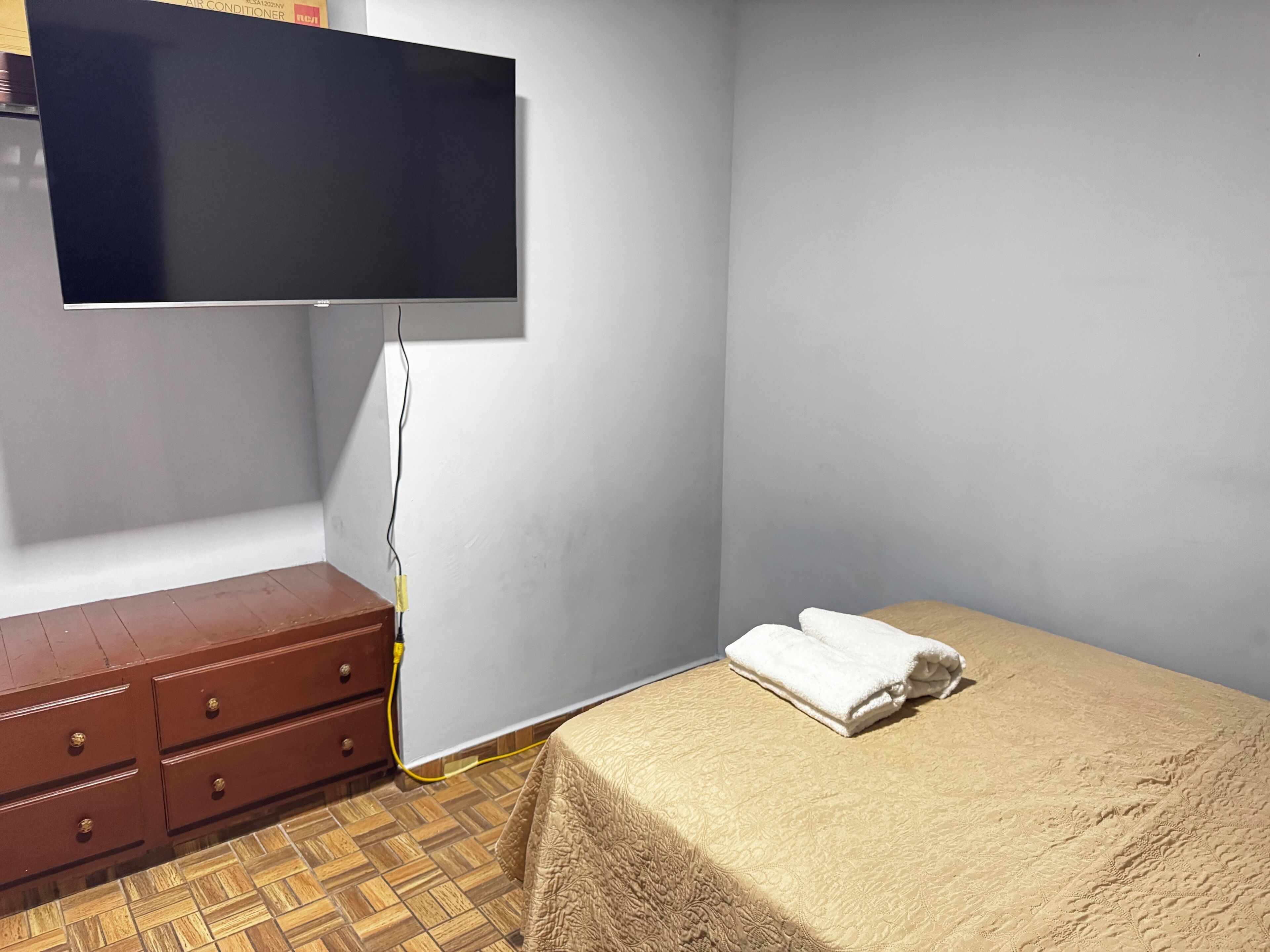 A bedroom with a bed, a dresser, and a TV mounted on the wall.
