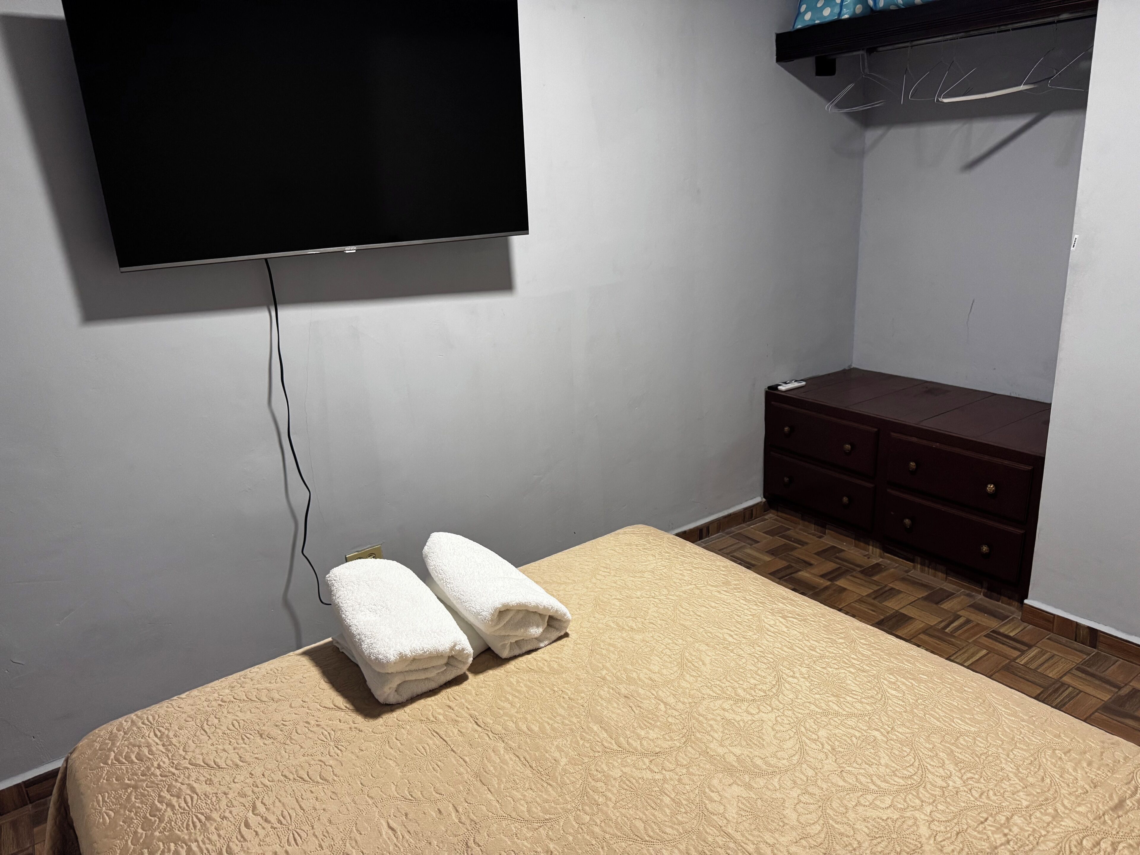 A bedroom with a bed, a dresser, and a TV mounted on the wall.