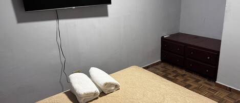 A bedroom with a bed, a dresser, and a TV mounted on the wall.